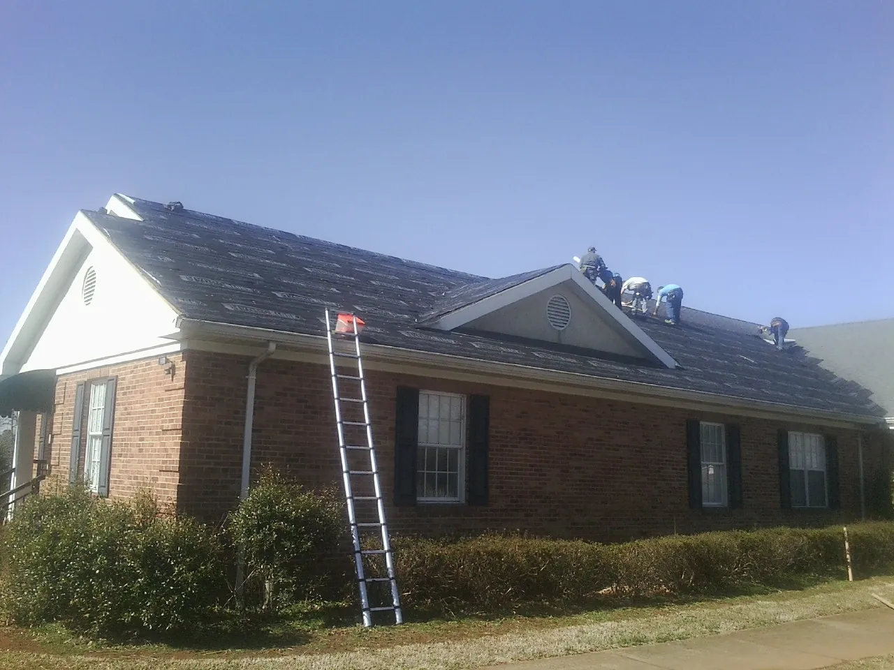 Crew tearing shingles off a brick ranch roof with a ladder set — Metal Roof Repair work by our crew in Little Plymouth