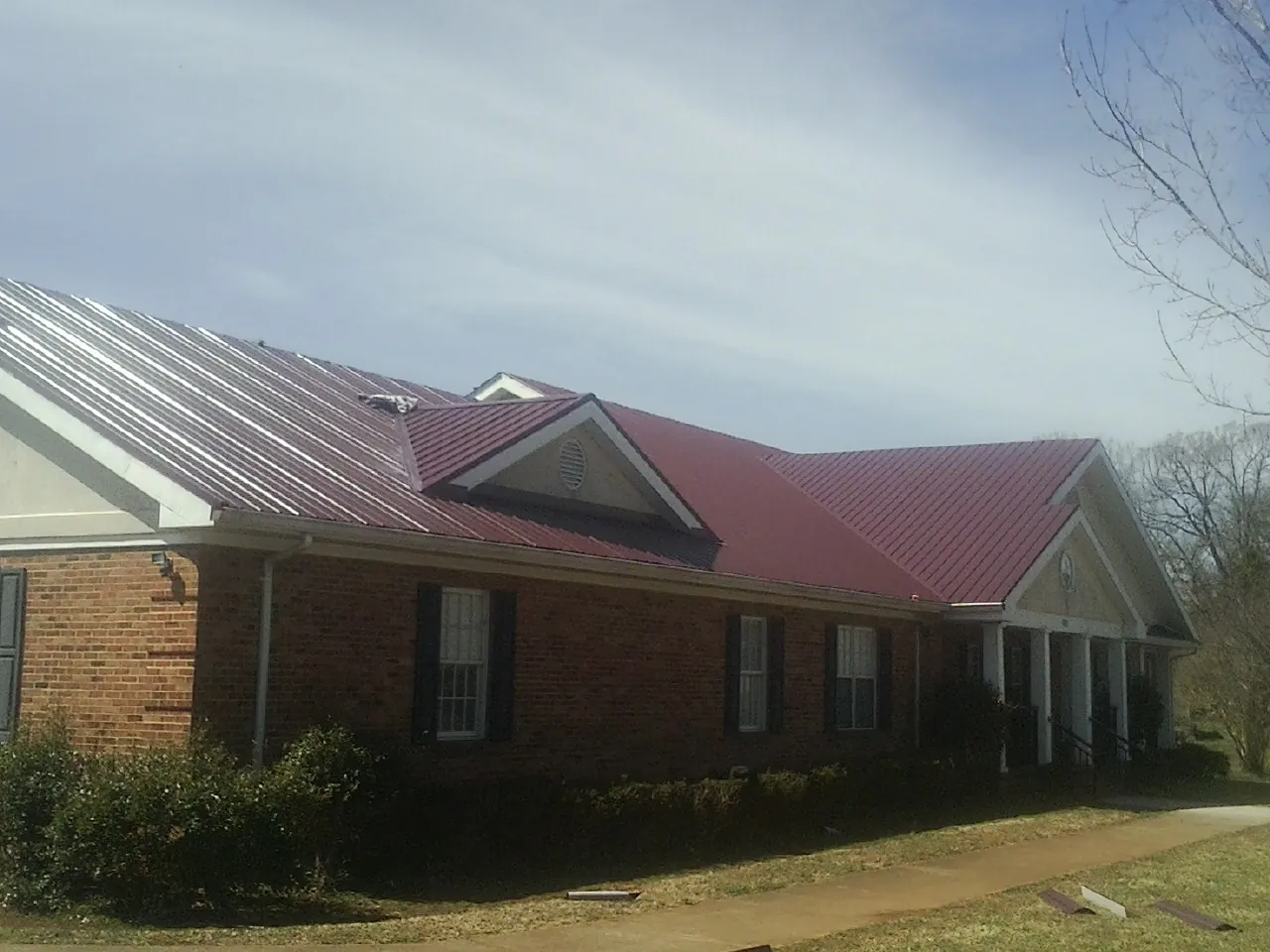 Red metal roof with gabled entries on a long brick building, from a Hail Damage Roof Repair job in Little Plymouth
