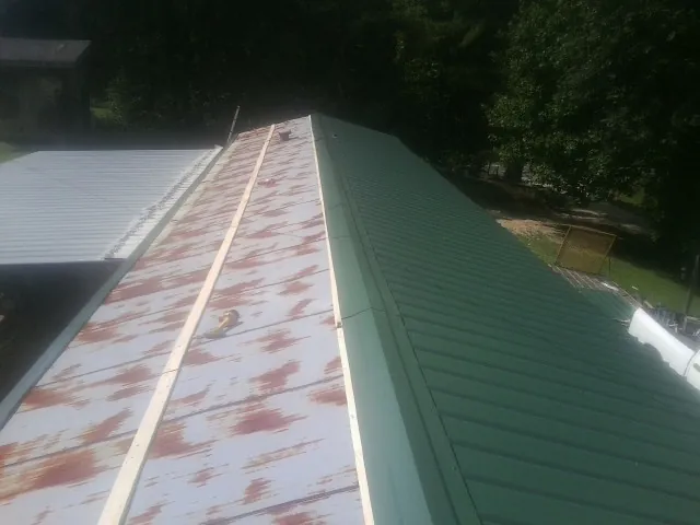 Old rusted panels beside newly installed green metal roofing — Wind Damage Roof Repair by Roofing Brothers in Little Plymouth