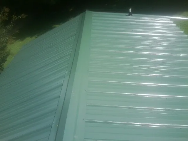 New green metal panels meeting at the ridge of a roof — Flat Roof Repair work by our crew in Little Plymouth