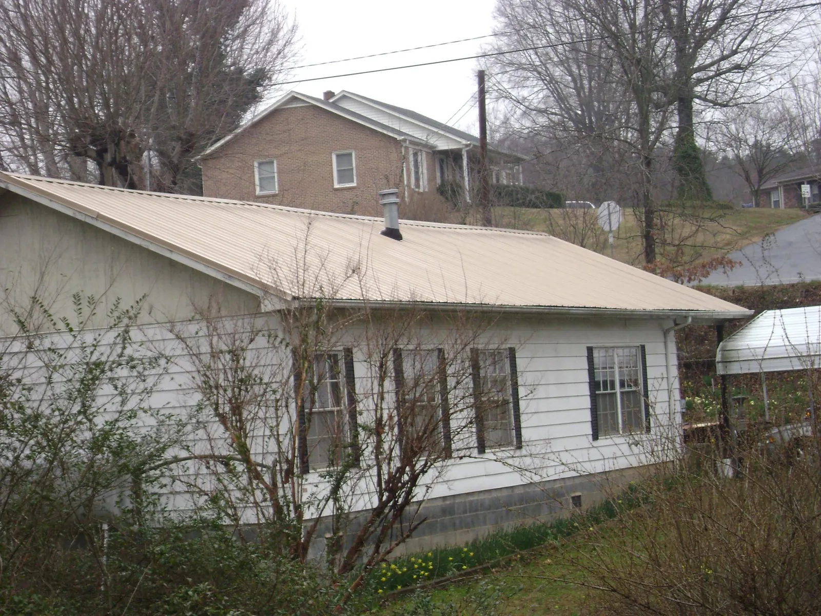 Tan metal roof on a white sided house set into a hillside — Commercial Roofing by Roofing Brothers in Little Plymouth
