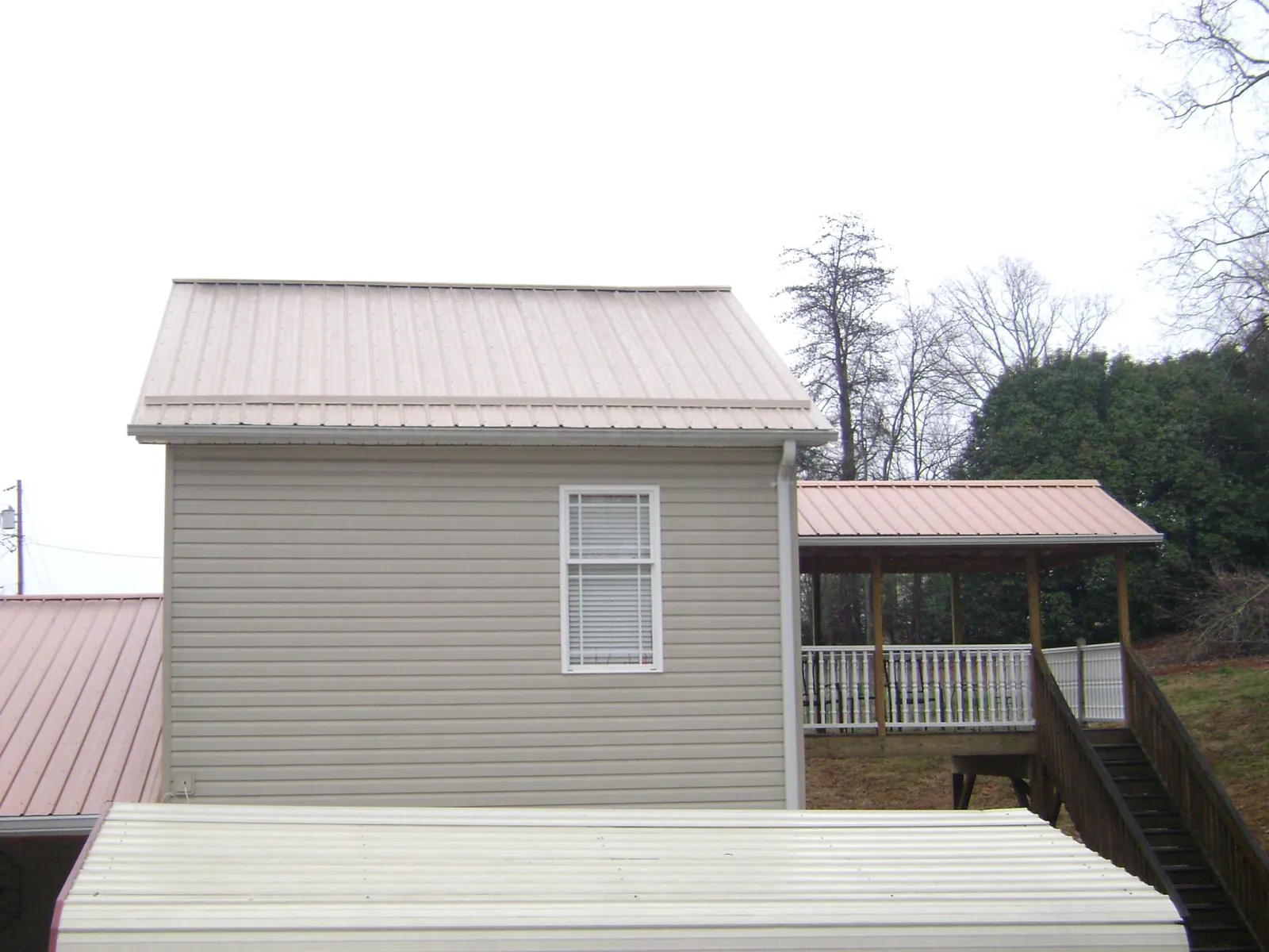 Tan metal roofs on a two story addition and attached porch, from a Roof Replacement job in Little Plymouth